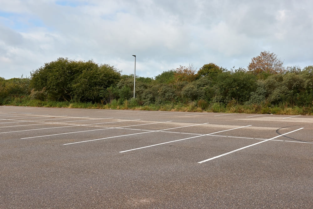 Large empty asphalt parking lot with fresh white line markings beside a row of trees under a cloudy sky.